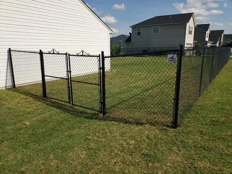 Black chain link fence with a double gate around a back yard beside a cream house