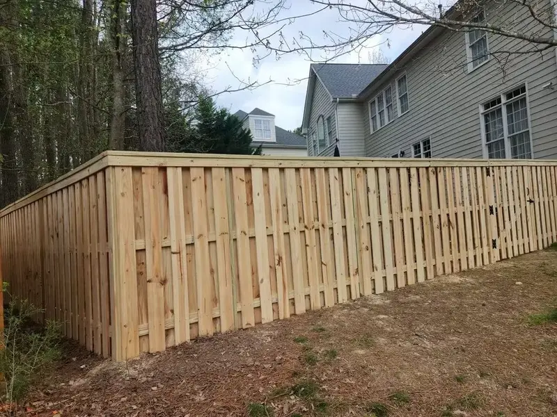 Finished board-on-board wood privacy fence in a wooded yard with houses behind