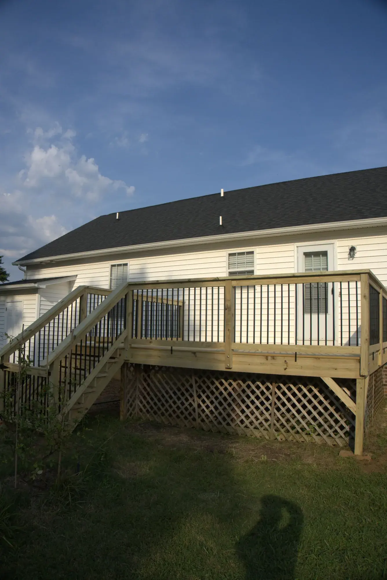 Finished wood deck along the back of a cream house with a full railing of black balusters, side stairs and lattice skirting