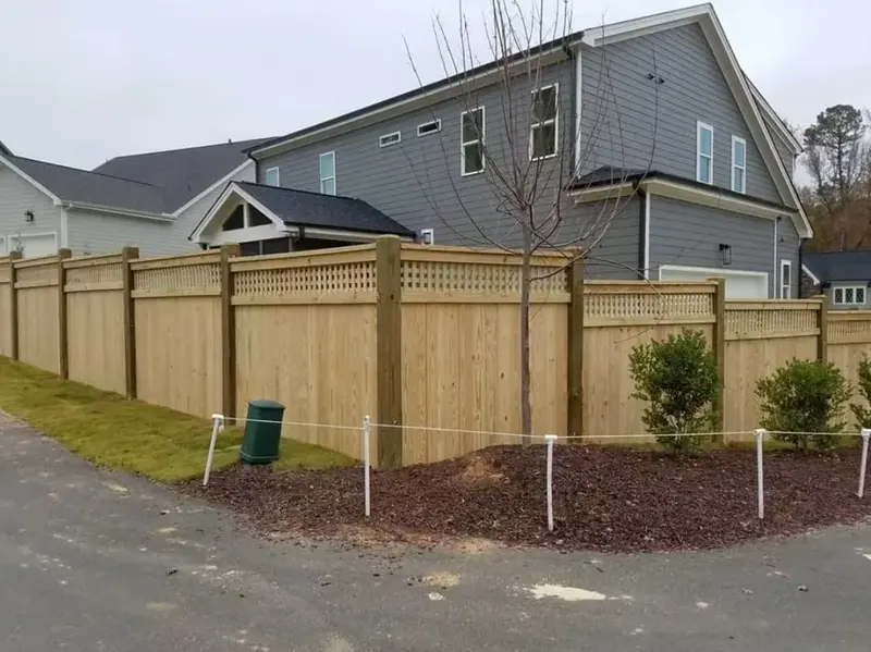 Finished wood privacy fence with lattice top along a driveway, grey house behind