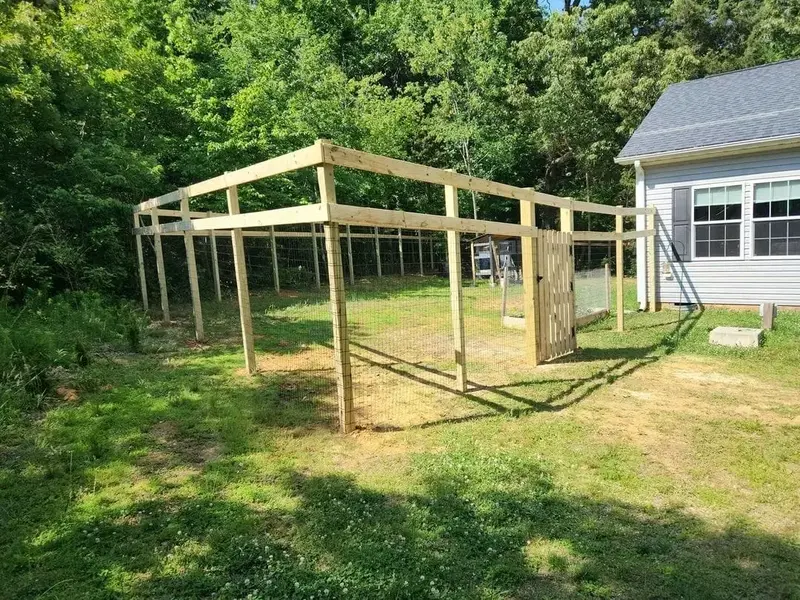 Wood-framed mesh fence going up, posts and top rails set, gate hung, mesh not yet on