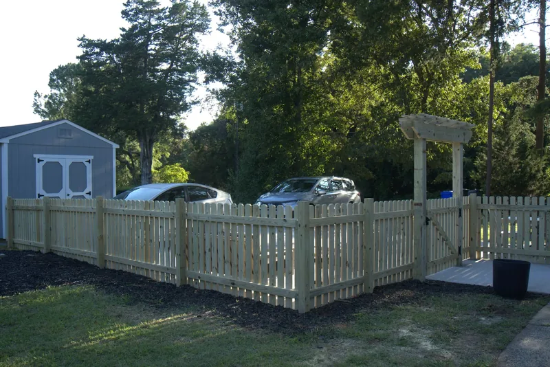 Finished wood picket fence with an arbor gate running past a grey storage shed