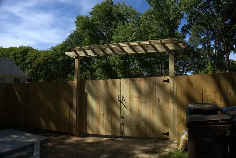 Wood privacy fence with a double gate under a pergola arbor