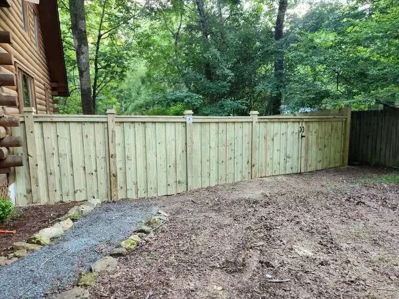 Finished wood privacy fence with a gate beside a log cabin house