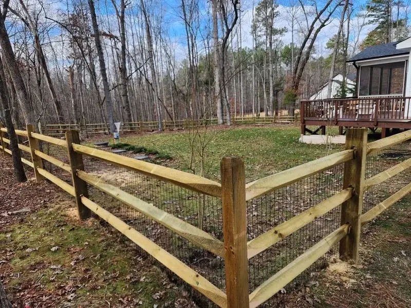Finished split-rail fence with wire mesh around a wooded yard, screened porch and deck behind