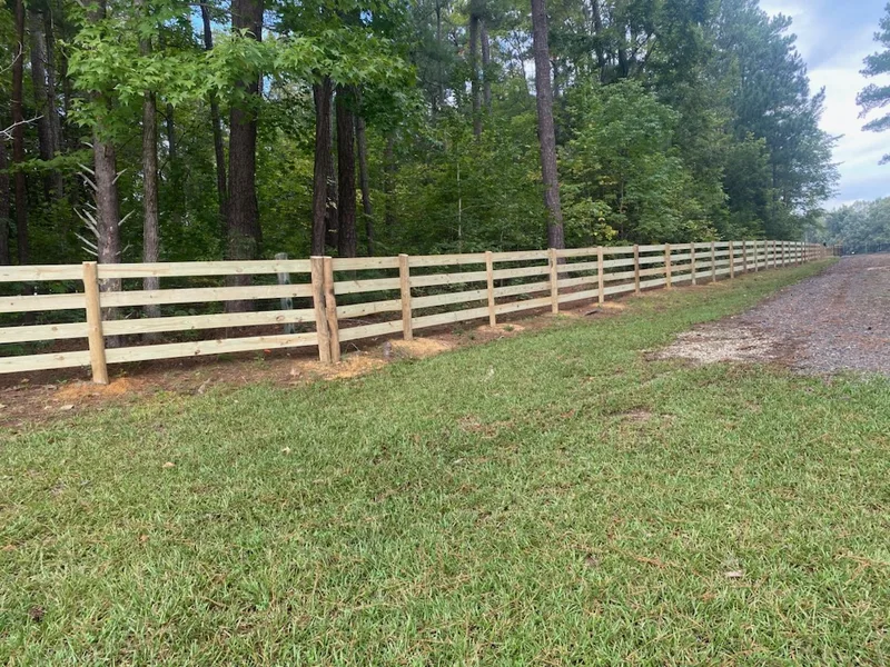 Wood rail farm fence running along a gravel drive at the edge of the woods