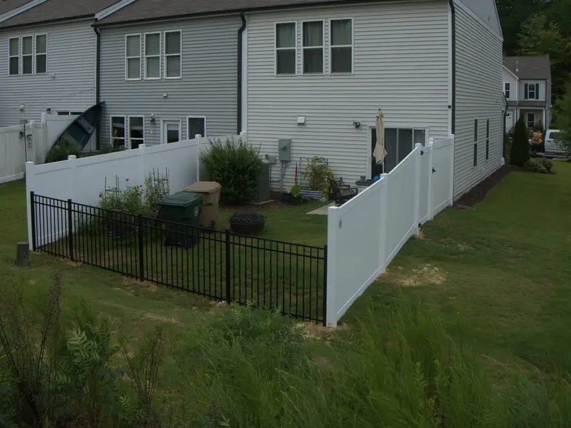 White vinyl privacy fence meeting a black aluminum fence behind a row of townhomes
