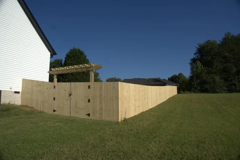 Finished wood privacy fence with a pergola built over the double gates